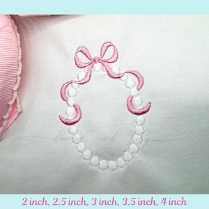 May include: An embroidered design of a pink bow and a pearl necklace on a white background. The text at the bottom reads: 2 inch, 2.5 inch, 3 inch, 3.5 inch, 4 inch. The design is likely for a craft project.