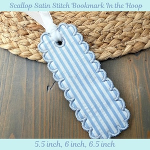 Puede incluir: Marcapáginas a rayas azules y blancas con borde festoneado y cinta blanca. El marcapáginas mide aproximadamente 14, 15 o 16.5 cm de largo. El texto "Scallop Satin Stitch Bookmark In the Hoop" está en la parte superior.