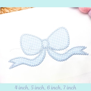 May include: A white fabric with a large, light blue gingham bow applique. The bow has a scalloped edge and flowing ribbons. Text at the bottom reads "4 inch, 5 inch, 6 inch, 7 inch".
