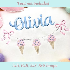 May include: White fabric embroidered with the name "Olivia" in light blue script. A garland of three ice cream cones with pink ice cream and sprinkles hangs below the name, with pink bows on each side. Text at the top reads "Font not included".