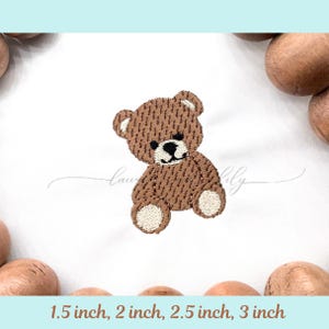 May include: Embroidered brown teddy bear design on white fabric. The bear has a black nose and eyes, with beige accents on the paws and ears. The text "Lau & Lily" is written in cursive. The image also includes the text "1.5 inch, 2 inch, 2.5 inch, 3 inch".
