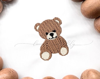 以下が含まれることがあります： 白い生地に刺繍された茶色のテディベアのデザイン。クマは黒い鼻と目をしており、足と耳にはベージュのアクセントがあります。「Lau & Lily」の文字が筆記体で書かれています。画像には「1.5 inch, 2 inch, 2.5 inch, 3 inch」の文字も含まれています。