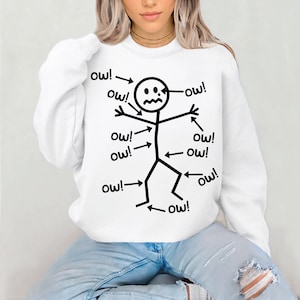 Puede incluir: Sudadera blanca con un dise&ntilde;o de figura de palo negro. La figura de palo tiene la palabra "&iexcl;ay!" apuntando a diferentes partes de su cuerpo, con una expresi&oacute;n angustiada.