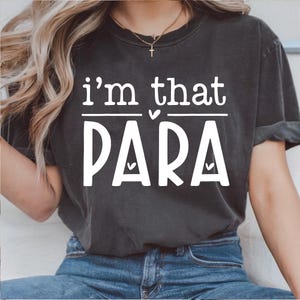 Puede incluir: Camiseta gris oscuro con el texto blanco "i'm that PARA". La camiseta tiene cuello redondo y mangas cortas. El texto está centrado en la parte delantera de la camiseta.