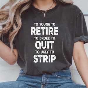May include: Dark gray t-shirt with the white text "TO YOUNG TO RETIRE TO BROKE TO QUIT TO UGLY TO STRIP." The shirt is a crew neck and has short sleeves. The model is wearing blue jeans.