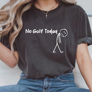 以下が含まれることがあります： 「No Golf Today」の文字と、悲しそうな顔の棒人間イラストがプリントされたダークグレーのTシャツ。カジュアルなスタイルで、普段使いに適しています。
