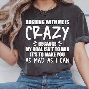 May include: Dark gray t-shirt with the text "ARGUING WITH ME IS CRAZY BECAUSE MY GOAL ISN'T TO WIN IT'S TO MAKE YOU AS MAD AS I CAN" in white lettering. The shirt is made of a soft material.