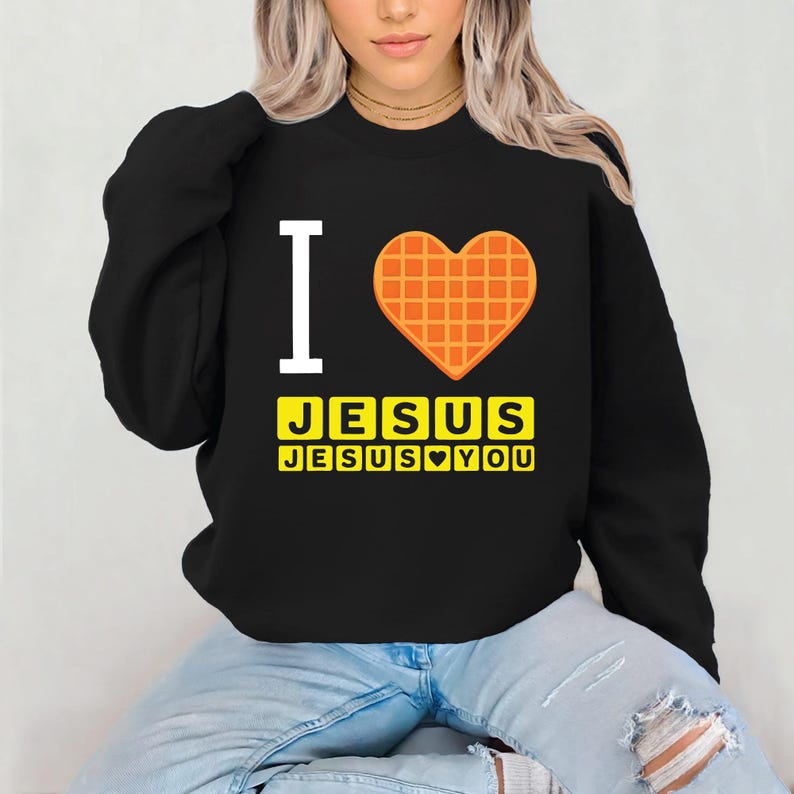 Puede incluir: Sudadera negra con el texto "I" y un coraz&oacute;n de gofre. Debajo del coraz&oacute;n, el texto "JESUS" se muestra en letras amarillas, con "JESUS YOU" debajo.