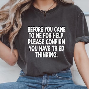 May include: Dark gray t-shirt with the white text: "BEFORE YOU CAME TO ME FOR HELP, PLEASE CONFIRM YOU HAVE TRIED THINKING." The shirt is a casual style, suitable for everyday wear.