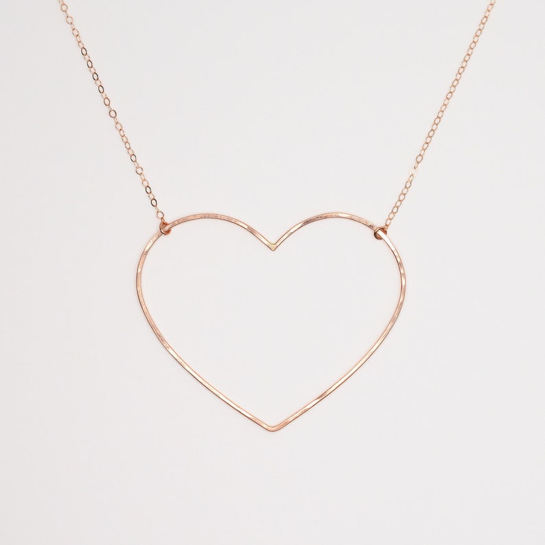 May include: A rose gold heart-shaped pendant necklace. The pendant is a large, open heart design suspended from a delicate chain. The necklace is displayed against a white background, highlighting the jewelry's simple elegance.