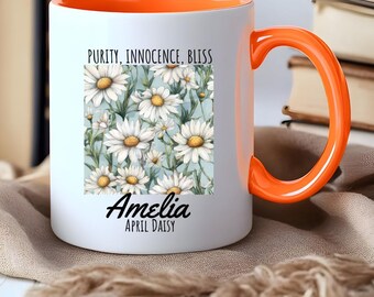 Könnte beinhalten: Eine weiße Keramiktasse mit orangefarbenem Rand und Henkel. Die Tasse zeigt ein Blumenmuster mit weißen Gänseblümchen auf hellblauem Hintergrund. Der Text "Purity, Innocence, Bliss" ist über dem Blumenmuster gedruckt. Der Name "Amelia" ist unter dem Blumenmuster gedruckt, mit dem Text "April Daisy" darunter.