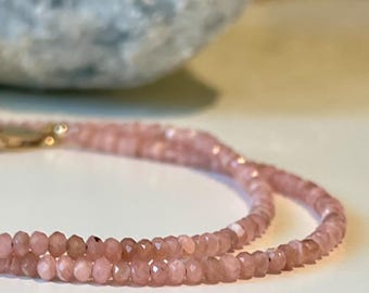 May include: A delicate pink gemstone necklace with a gold clasp. The necklace is composed of small, faceted beads, creating a subtle sparkle. The soft pink color and intricate design suggest a piece of fine jewelry.