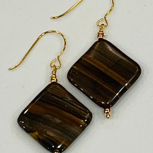 May include: A pair of gold earrings with brown and gold tiger's eye gemstone pendants in a diamond shape.