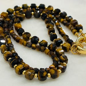 May include: A double-strand necklace made of brown and black tiger's eye beads with gold accents. The necklace has a gold clasp.