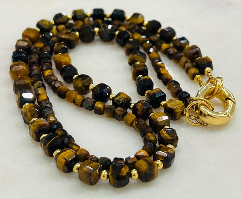 May include: A double-strand necklace made of brown and black tiger's eye beads with gold accents. The necklace has a gold clasp.