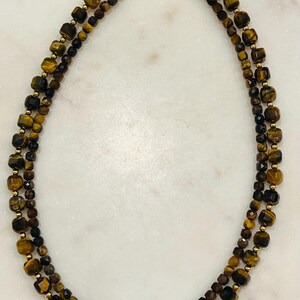 May include: A gold necklace with two strands of tiger's eye and black beads.