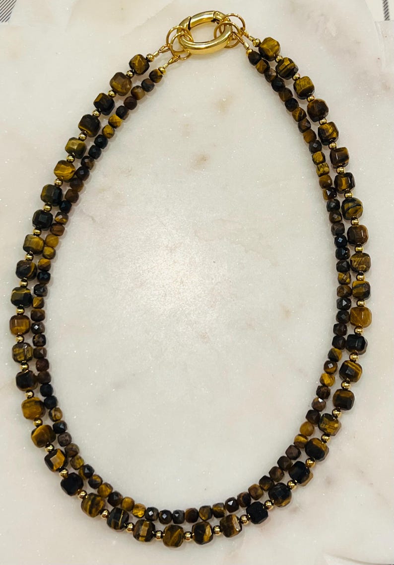 May include: A gold necklace with two strands of tiger's eye and black beads.