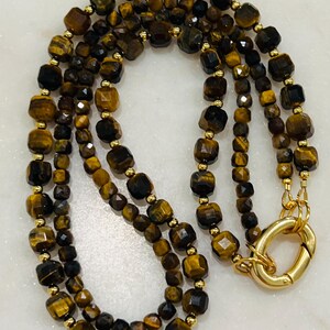 May include: A gold chain necklace with multiple strands of brown and gold tiger's eye beads. The necklace has a gold clasp.