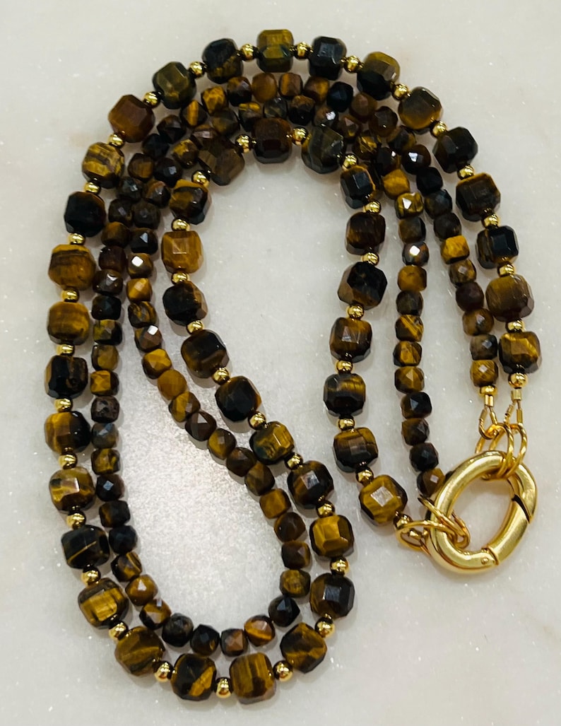 May include: A gold chain necklace with multiple strands of brown and gold tiger's eye beads. The necklace has a gold clasp.