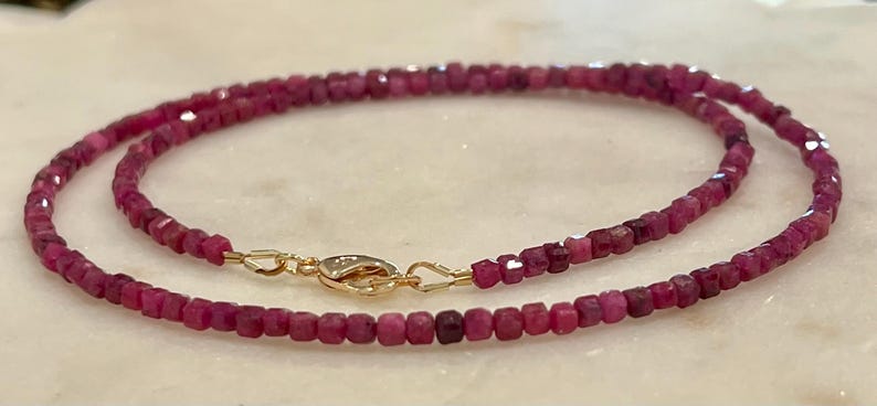 Puede incluir: Un delicado collar con peque&ntilde;as cuentas de rub&iacute; facetadas en un tono rosa intenso. El collar est&aacute; ensartado con un cierre dorado. Las cuentas son de tama&ntilde;o uniforme y crean una hebra continua y elegante.