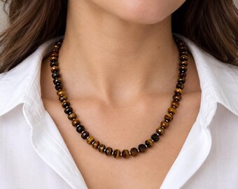 May include: A necklace featuring round, faceted tiger's eye beads in shades of brown and gold, interspersed with small, polished silver-toned metal spacer beads. The beads are arranged in a single strand, creating a consistent pattern around the neck.