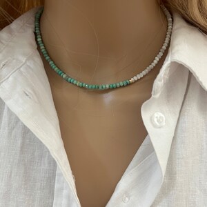 May include: A delicate, two-toned necklace with green and white beads. The necklace is made of small, round beads and is strung on a gold chain.