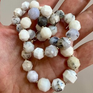 May include: A beaded necklace featuring faceted, irregular-shaped beads in shades of white, gray, and pale blue. The beads are strung together with gold-colored connectors, creating a delicate and elegant piece of jewelry.