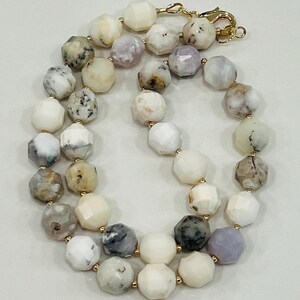 May include: A gemstone necklace featuring faceted, multi-colored beads in shades of white, gray, and lavender. The beads are strung together with gold-colored connectors and a clasp.