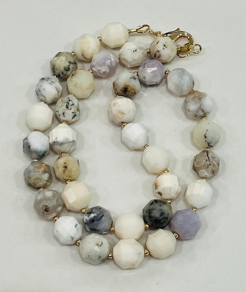 May include: A gemstone necklace featuring faceted, multi-colored beads in shades of white, gray, and lavender. The beads are strung together with gold-colored connectors and a clasp.