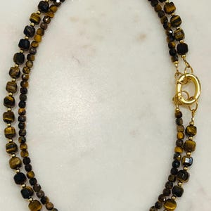 May include: A double-strand necklace made with gold-toned beads and tiger's eye stones. The necklace has a gold-toned clasp.