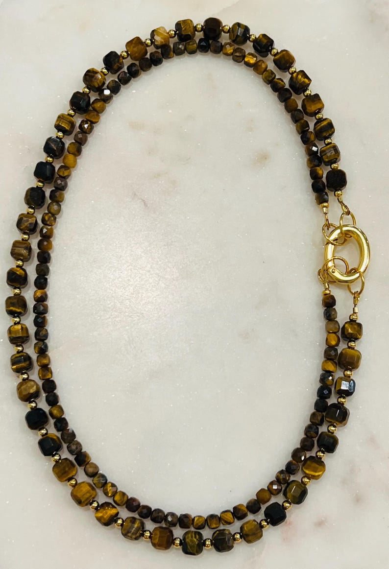 May include: A double-strand necklace made with gold-toned beads and tiger's eye stones. The necklace has a gold-toned clasp.