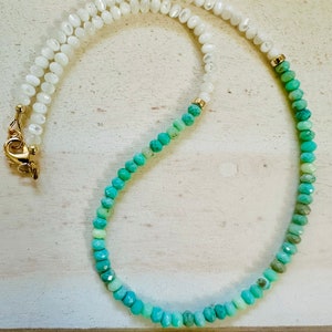 May include: A white and green ombre beaded necklace with a gold clasp. The necklace is made of small, round beads.