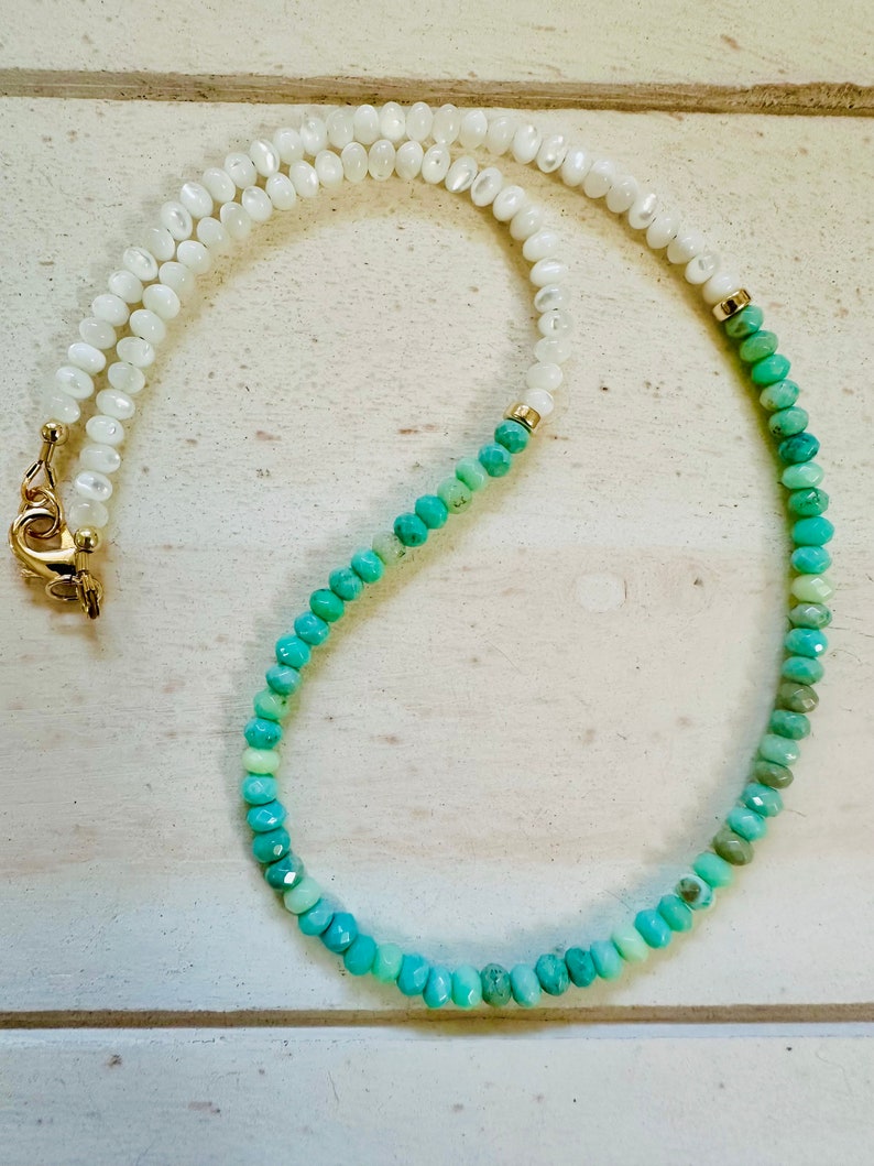 May include: A white and green ombre beaded necklace with a gold clasp. The necklace is made of small, round beads.