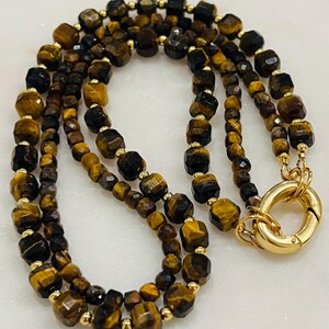 May include: A double-strand necklace made with tiger's eye beads and gold accents. The necklace has a gold clasp.