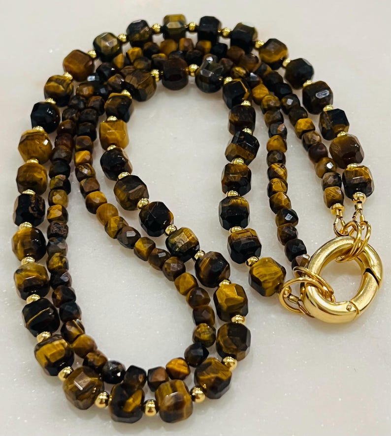 May include: A double-strand necklace made with tiger's eye beads and gold accents. The necklace has a gold clasp.