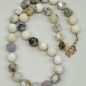 May include: A faceted gemstone necklace featuring a variety of colors including white, gray, and lavender. The necklace has a gold-colored clasp and small gold-colored beads between each gemstone. The gemstones are approximately 0.5 inches in diameter.