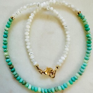 May include: A delicate necklace with a gradient of turquoise and white beads. The necklace is made with small, faceted beads and has a gold clasp.
