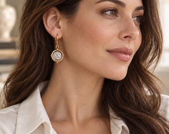 May include: A gold-toned drop earring featuring a circular pendant with a silver-colored coin-style center. The coin is framed by a gold-toned border with small decorative prongs, suspended from a simple gold-toned hoop earring mechanism.