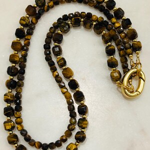 May include: A double-strand necklace made with tiger's eye beads. The beads are faceted and have a gold-toned metal clasp.