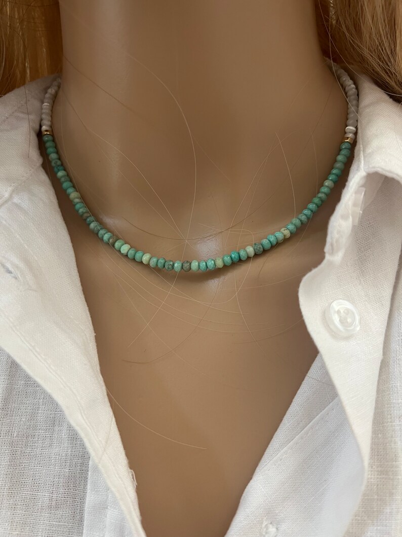 May include: A turquoise and white beaded necklace on a mannequin. The necklace is made of small, round beads.