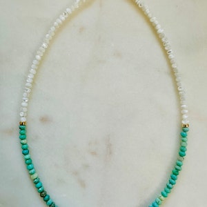 May include: A white and turquoise gemstone necklace with a gold clasp. The necklace is made of small, round beads that are strung together in a graduated pattern. The white beads are at the top of the necklace, and the turquoise beads are at the bottom.