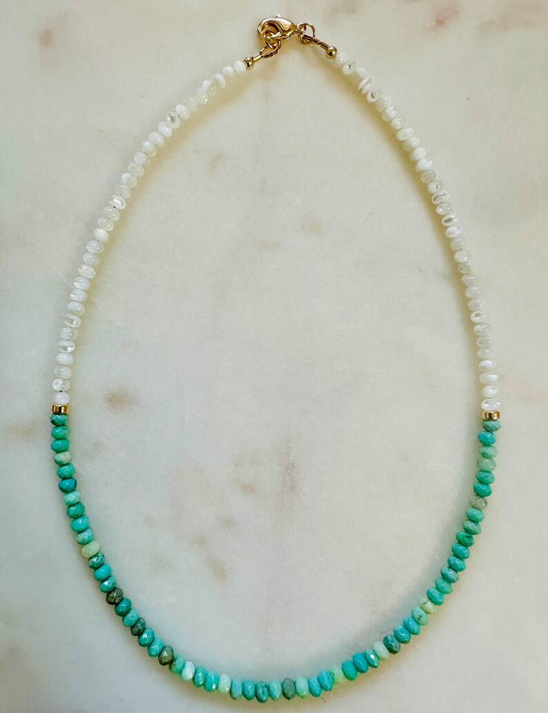 May include: A white and turquoise gemstone necklace with a gold clasp. The necklace is made of small, round beads that are strung together in a graduated pattern. The white beads are at the top of the necklace, and the turquoise beads are at the bottom.