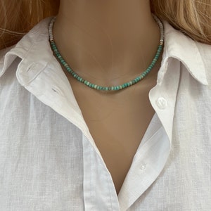 May include: A turquoise and white beaded necklace with a gold clasp. The necklace is on a white mannequin.