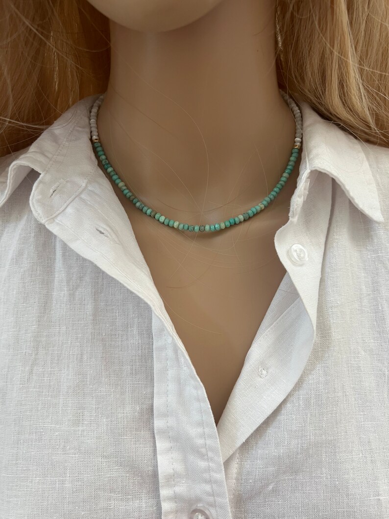 May include: A turquoise and white beaded necklace with a gold clasp. The necklace is on a white mannequin.