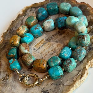 May include: A turquoise stone necklace with a gold clasp. The necklace features large, irregular turquoise beads in shades of blue, green, and brown. The gold clasp adds a touch of elegance to the handcrafted jewelry.