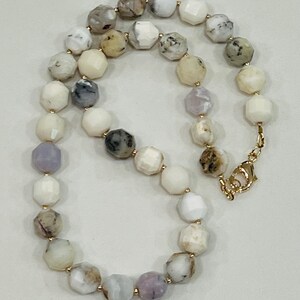 May include: A faceted bead necklace featuring a variety of colors including white, gray, and lavender. The beads are strung together with gold-colored clasps and connectors. The necklace is displayed on a neutral background.