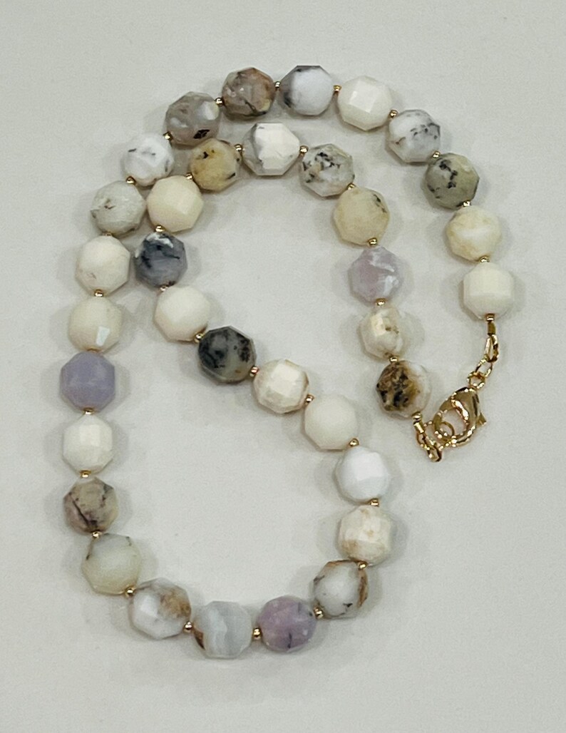 May include: A faceted bead necklace featuring a variety of colors including white, gray, and lavender. The beads are strung together with gold-colored clasps and connectors. The necklace is displayed on a neutral background.
