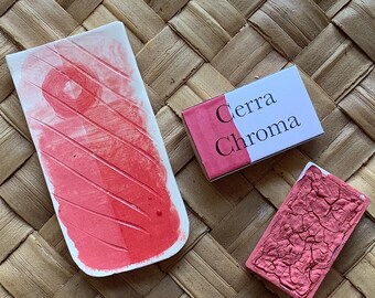 Può includere: Tre pastiglie di acquerello rosa, due sono rettangolari e una è una pastiglia ovale più grande. Le pastiglie rettangolari hanno il testo "Cerra Chroma" stampato su di esse. Le pastiglie sono su una superficie intrecciata di colore marrone chiaro.