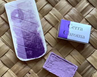 Può includere: Una tavolozza di acquerello viola con un'etichetta bianca che dice "Cerra Chroma". La tavolozza è su un tappetino intrecciato.