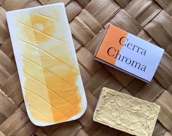 May include: A close-up of a watercolour pan with a yellow pigment. The pan is labelled "Cerra Chroma".